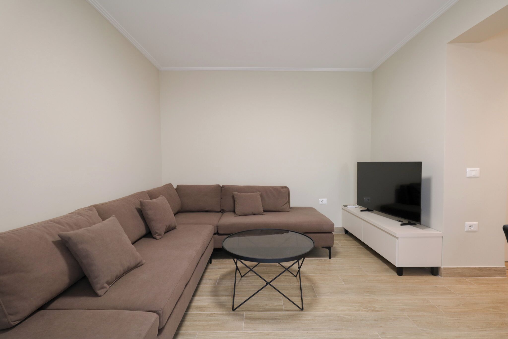 A modern living room with a sectional sofa, a glass coffee table, and a flat-screen TV on a white cabinet.