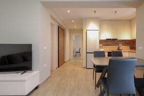Una sala de estar moderna con televisor de pantalla plana, un comedor con mesa y sillas, y una cocina con gabinetes de madera y cafetera.