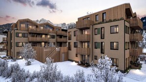 Ein mehrgeschossiges Gebäude mit Balkonen und großen Fenstern, umgeben von schneebedeckten Bäumen und Bergen im Hintergrund.