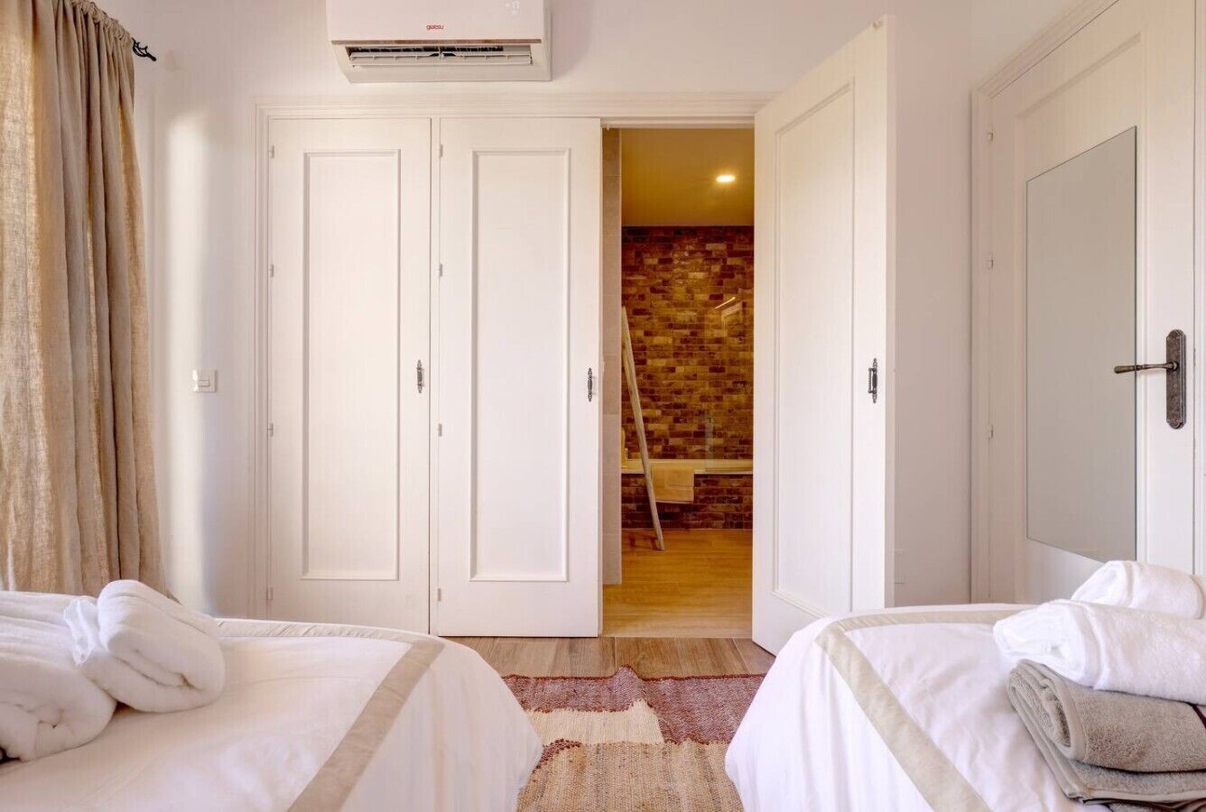 A hotel room with two beds, a brick wall, and a wooden floor.