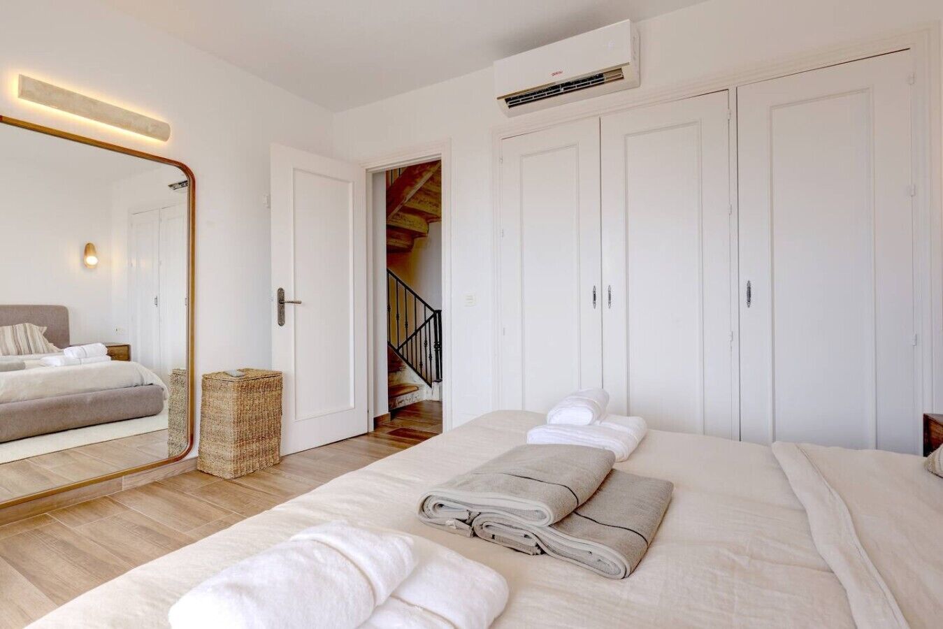 Een slaapkamer met een bed, een grote spiegel, een kledingkast en een trap naar een verdieping boven.