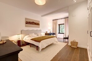 Ein Schlafzimmer mit Bett, Nachttischen, Schreibtisch, Stuhl, einem Fenster mit Vorhängen und einem Bild an der Wand.