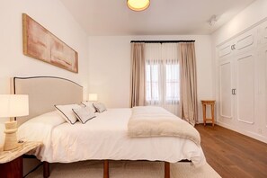 Une chambre à coucher comprenant un lit, des lampes de chevet, une table de chevet, une fenêtre avec des rideaux et une armoire.