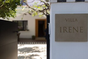 Ein Schild mit der Aufschrift 'VILLA IRENE' an einer weißen Wand, das den Namen eines Objekts angibt.