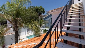 Una terraza en la azotea con piscina, palmeras y una escalera.