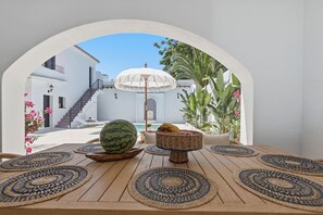 An outdoor seating area with a table, a watermelon, and a basket, overlooking a white building with a staircase and a pool. - Villa Irene · Heated Pool · Pedregalejo (Málaga)