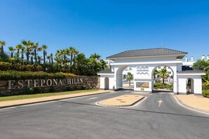 Ein verschlossenes Tor mit einem Schild, auf dem 'ESTEPONA HILLS' steht, und ein weißer Bogen mit dekorativen Elementen.