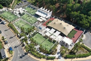 Luchtbeeld van een sportcomplex met meerdere tennisbanen, een overdekt zitgedeelte en een aangelegde omgeving.