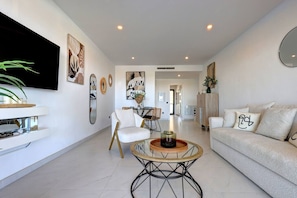 A modern living room with a sofa, armchair, coffee table, and artwork on the walls. - Estepona Hills Luxury Resort 3-Bedroom Apartment (Estepona)