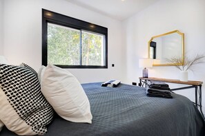 Ein Schlafzimmer mit Bett, Fenster, Nachttisch mit Lampe und Spiegel.