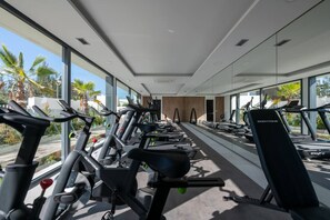 A gym with rows of stationary bikes and treadmills, large windows, and a view of palm trees. - Sky Penthouse with Private Pool (Artola)