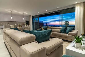 Ein modernes Wohnzimmer mit einer Sofagarnitur, einem Couchtisch und einem großen Fenster mit Blick auf den Himmel.
