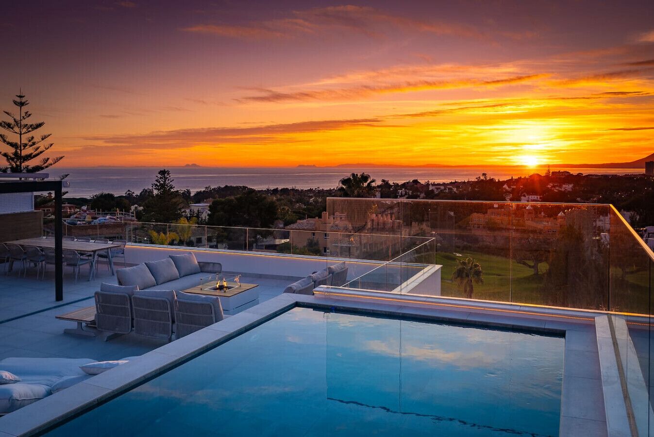 A rooftop infinity pool with outdoor seating and a sunset view.