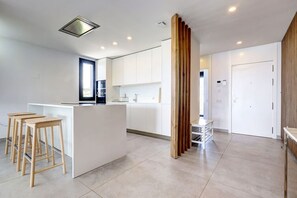 A modern kitchen with white cabinetry, a central island, and wooden stools. - Duplex Penthouse · Sea & Sky · Artola Alta (Marbella)