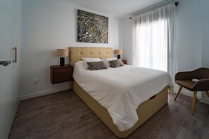 A bedroom with a large bed, two bedside tables, a chair, a painting on the wall, and a window with curtains. - Charming Townhouse in Cancelada Village (Cancelada)