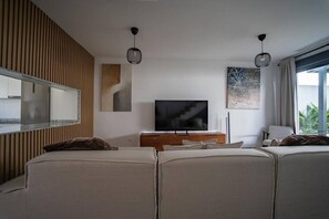 Uma sala de estar moderna com televisão de tela plana, uma parede de destaque em madeira, uma janela grande com cortinas e um sofá.
