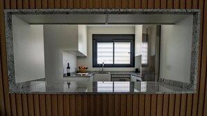 A modern kitchen with a central island, a window with blinds, and a wooden panel border. - Charming Townhouse in Cancelada Village (Cancelada)