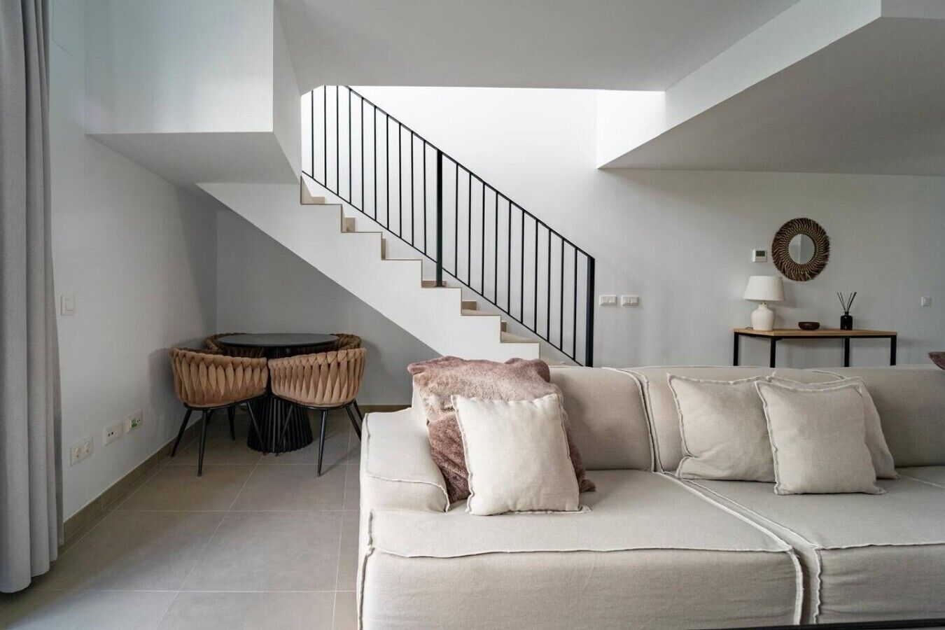 Ein modernes Wohnzimmer mit Sofa, Esstisch mit Stühlen, einer Treppe und einem kleinen Tisch mit Lampe und Dekoration.