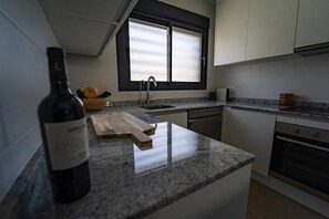 A kitchen with a granite countertop, a wine bottle, a cutting board, a sink, and a window with blinds. - Charming Townhouse in Cancelada Village (Cancelada)