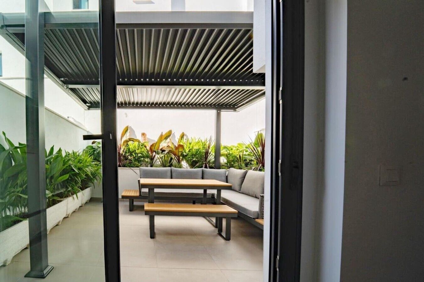 An indoor patio area with a seating arrangement, including a sofa and a table, surrounded by potted plants.