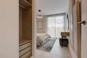 Ein Schlafzimmer mit Bett, Nachttisch, Lampe, einem Fenster mit Vorhängen und einem Kleiderschrank.