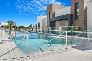 Ein Schwimmbecken mit modernem Design, umgeben von einem Glasgeländer und wolkenlosem Himmel.