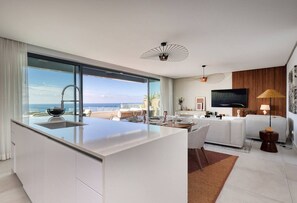 Een moderne keuken met een groot eiland, een zithoek met een bank en tafel, een flatscreen televisie en uitzicht op de oceaan.