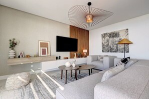 Ein modernes Wohnzimmer mit Flachbildfernseher, rundem Couchtisch, grauem Sofa und einer außergewöhnlichen Deckenleuchte.