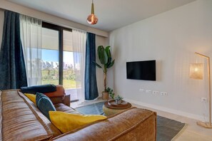 A modern living room with a sofa, a television, a plant, and a view of the outdoors. - PAZ House with Views and a Garden (Málaga)