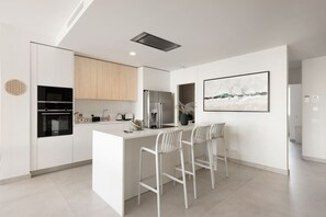 Eine moderne Küche mit weißen Schränken, einer zentralen Kochinsel mit Barhocker und einem großen, gerahmten Kunstwerk an der Wand.