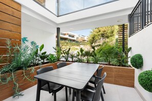 A modern patio with a dining table and chairs, surrounded by various plants and a view of buildings in the background. - Venere Retreat: Serenity and Design (Marbella)