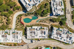 An aerial view of a residential area with modern buildings, a curved road, and a central swimming pool. - Venere Retreat: Serenity and Design (Marbella)