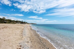 Ein Strand mit klarem Wasser, sandigem Ufer und einer fernen Küstenlinie mit Gebäuden.