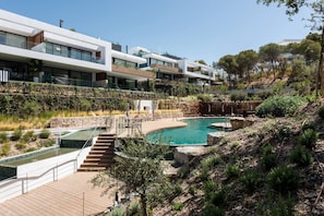 Ein modernes Gebäude mit Poolbereich, einschließlich eines kleinen Pools und eines größeren Pools mit Wasserfall.