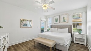 Quarto com cama, banco, ventilador de teto e obras de arte nas paredes.