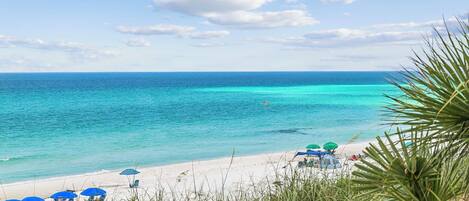 A beach with clear turquoise water, white sand, and a few umbrellas.