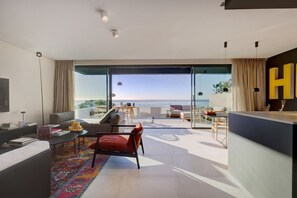 Ein modernes Wohnzimmer mit einem großen Glasfenster, das auf einen Balkon mit Meerblick führt.