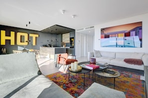 A modern living room with a sofa, a coffee table, and a colorful rug. There is a kitchen area with a bar and a dining table. A large painting is on the wall. - Penthouse with ocean views and a private pool (Marbella)