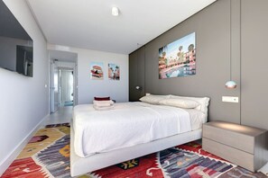 Ein modernes Schlafzimmer mit einem großen Bett, einem Nachttisch, einem an der Wand montierten Fernseher und einem farbenfrohen Teppich.