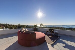 A rooftop terrace with a red cushioned seating area, a small round table, and a potted plant. - Penthouse with ocean views and a private pool (Marbella)