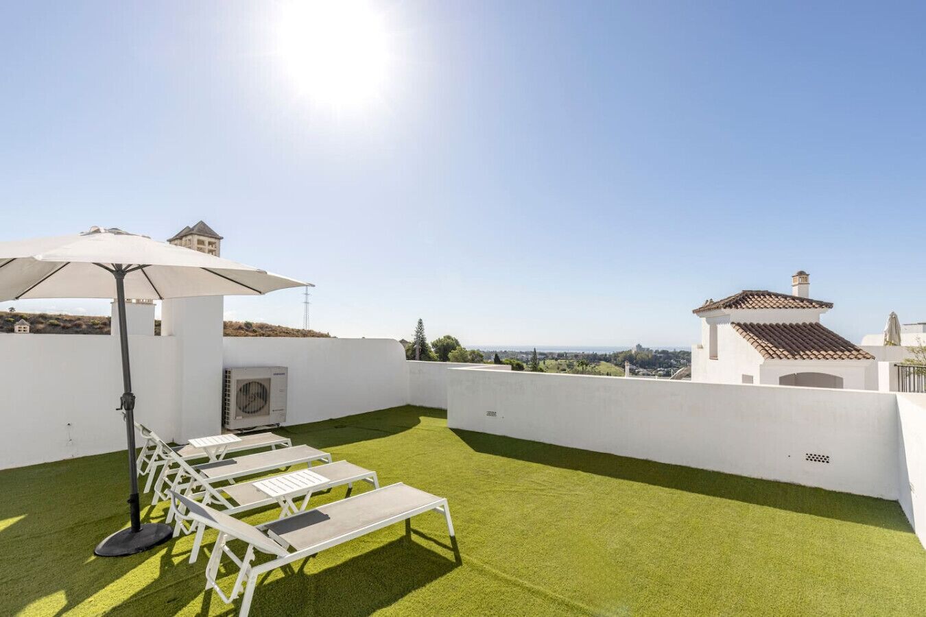 A rooftop terrace with artificial grass, sun loungers, and a large umbrella.