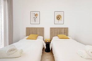 Habitación de hotel con dos camas, ropa de cama blanca, almohadas amarillas y dos cuadros en la pared.