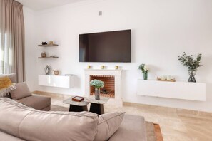 Ein modernes Wohnzimmer mit einem an der Wand montierten Flachbildfernseher über einem Kamin, einem beigen Sofa und einem Couchtisch mit dekorativen Accessoires.