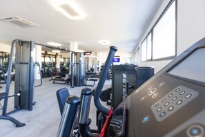 Ein Fitnessraum mit Trainingsgeräten, einer Steuerung und einer fensterdurchbrochenen Wand.