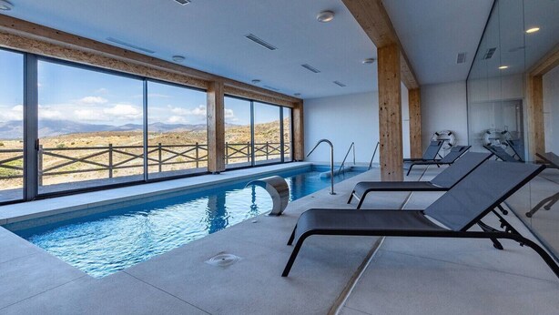An indoor swimming pool with clear views of the surrounding landscape, wooden beams on the ceiling, and lounge chairs. - Luxury Family Penthouse, 7 Pools, Ocean View & Golf (Benahavís)