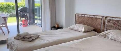 A modern bedroom with two beds, a large window, and a view of the outdoors.