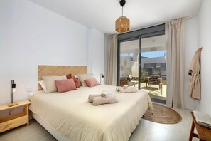 A bedroom with a large bed, a bedside table, a lamp, a window with curtains, and a view of the outside. - Modern apartment with a private garden (Málaga)