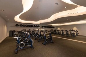 Ein Fitnessraum mit mehreren in Reihen angeordneten Trainingsrädern, einem Wandregal für Gewichte und einer Decke mit eingelassener Beleuchtung.