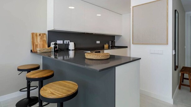 A modern kitchen with a central island, bar stools, and a large framed picture on the wall. - Modern apartment with a private garden (Málaga)