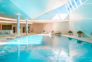 Ein Innenpool mit klarem, blauem Wasser, umgeben von Liegestühlen und Topfpflanzen.
